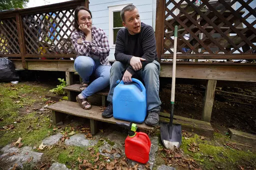 Lucinda Tyler and Aaron Raymo sit outside their home with fuel containers they used to fill their heating oil tank at their home, Wednesday, Oct. 5, 2022 in Jay, Maine. The couple shopped around for the best prices and bought heating oil 5 gallons at a time throughout the summer whenever they had any extra money. (AP Photo/Robert F. Bukaty)