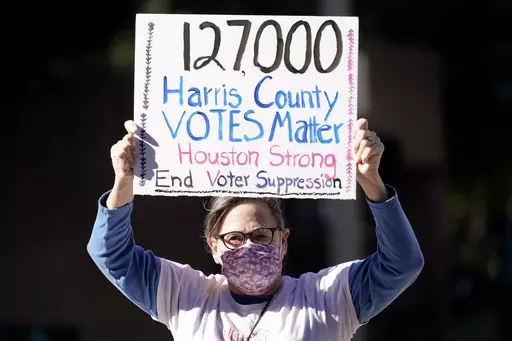 Demonstrator Gina Dusterhoft holds up a sign as she walks to join others standing across the street from the federal courthouse in Houston, Monday, Nov. 2, 2020, before a hearing in federal court involving drive-thru ballots cast in Harris County. (AP Photo/David J. Phillip, File)