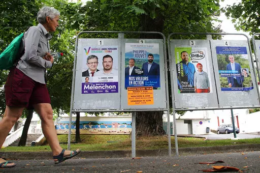 A woman walks past electoral posters of the upcoming parliamentary elections in Saint Jean de Luz, southwestern France, Wednesday June 8, 2022. The legislative elections will take place on June 12 and 19, 2022. (AP Photo/Bob Edme)
