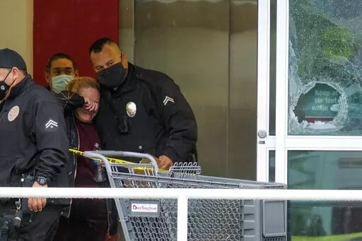 A police officer comforts a woman at the scene where two people were struck by gunfire in a shooting at a Burlington store as part of a chain formerly known as Burlington Coat Factory in North Hollywood, Calif., Thursday, Dec. 23, 2021. (AP Photo/Ringo H.W. Chiu)