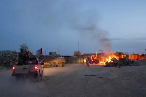 An Afghan National Army pickup truck passes parked U.S. armored military vehicles, as smoke rises from a fire in a trash burn pit at Forward Operating Base Caferetta Nawzad, Helmand province south of Kabul, Afghanistan, April 28, 2011. The Senate is expected to approve on Thursday a large expansion of health care and disability benefits for veterans of Iraq and Afghanistan in response to concerns about their exposure to toxic burn pits.  (AP Photo/Simon Klingert, File)