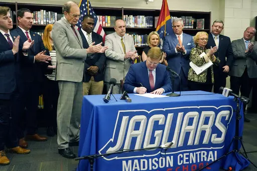 Flanked by lawmakers and educators, Mississippi Gov. Tate Reeves signs the teacher pay raise bill during a ceremonial bill signing, March 31, 2022, at Madison Central High School in Madison, Miss. (AP Photo/Rogelio V. Solis)