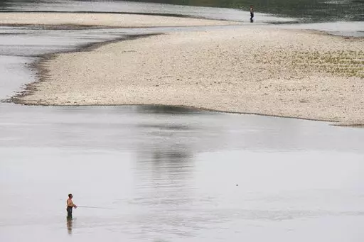 People fish near a hydroelectric power plant at Isola Serafini, on the Po river in San Nazzaro, Italy, Wednesday, June 15, 2022. The drying up of the river is jeopardizing drinking water in Italy's densely populated and highly industrialized districts and threatening irrigation in the most intensively farmed part of the country.  (AP Photo/Luca Bruno)