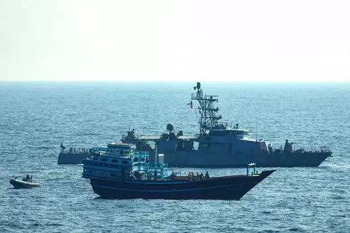 This photo released by the U.S. Navy, shows U.S. service members conduct a boarding on a stateless fishing vessel transiting international waters in the Gulf of Oman as a rigid-hull inflatable boat and patrol coastal ship USS Chinook (PC 9) sail nearby, Tuesday, Jan. 18, 2022. The U.S. Navy announced Sunday, Jan. 23 that it seized the boat in the Gulf of Oman carrying fertilizer used to make explosives that was caught last year smuggling weapons to Yemen. (U.S. Navy via AP)