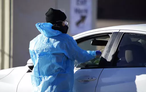 A medical technician performs a nasal swab test on a motorist queued up in a line at a COVID-19 testing site near All City Stadium Dec. 30, 2021, in southeast Denver. Millions of workers whose jobs don’t provide paid sick days are having to choose between their health and their paycheck as the omicron variant of COVID-19 rages across the nation. While many companies instituted more robust sick leave policies at the beginning of the pandemic, those have since been scaled back with the rollout o