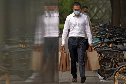 A man wearing a face mask to help protect from the coronavirus carries goody bags as he walks by a row of bicycles parked along a pavement in Beijing, Monday, Sept 13, 2021. (AP Photo/Andy Wong)