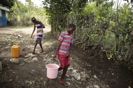 Siblings Mylouise Veillard, left, and Myson walk home with water they collected from a well, for cooking, cleaning and drinking, in a rural area of Saint-Louis-du-Sud, Haiti, Thursday, May 25, 2023. The siblings were considered “poverty orphans" for three years until they were reunited with their mother, Renèse Estève, who had dropped them off at an orphanage where she believed they'd get better care. Their mother brought them home after she was startled at the weight they had lost, convince