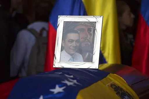 A framed portrait of opposition activist Fernando Alban shadowed by an image of Jesus Christ sits on the flag-draped casket containing his remains, during a solemn ceremony at the National Assembly headquarters, in Caracas, Venezuela, Tuesday, Oct. 9, 2018. A federal judge in Miami has awarded on September 2022,  $73 million in damages to Alban´s family who died while in custody in what he described as a “murder for hire” carried out by a criminal enterprise led by President Nicolas Maduro.
