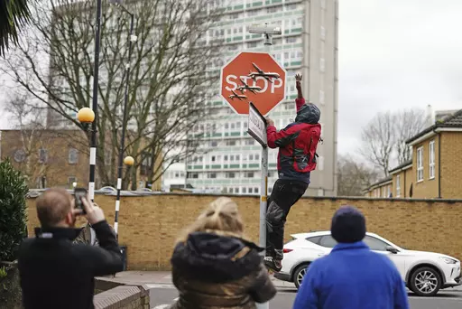 A person removes a piece of art work by Banksy, which shows what looks like three drones on a traffic stop sign, which was unveiled at the intersection of Southampton Way and Commercial Way in Peckham, south east London, Friday Dec. 22, 2023. (Aaron Chown/PA via AP)