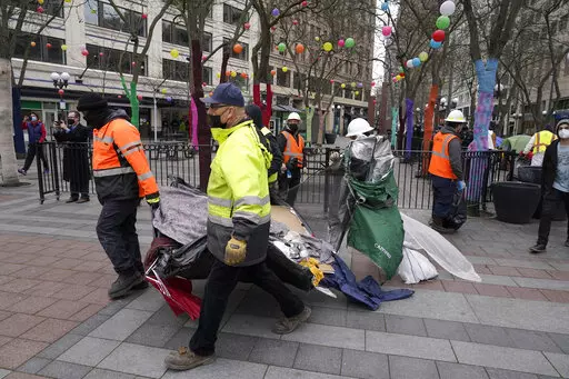 Workers carry a tent used by people experiencing homelessness to a garbage truck, Friday, March 11, 2022, during the clearing and removal of several tents at an encampment in Westlake Park in downtown Seattle. Increasingly in liberal cities across the country — where people living in tents in public spaces have long been tolerated — leaders are removing encampments and pushing other strict measures to address homelessness that would have been unheard of a few years ago. (AP Photo/Ted S. Warr