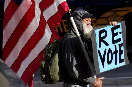 A man protests outside the Maricopa County Board of Supervisors auditorium prior to the board's general election canvass meeting, Nov. 28, 2022, in Phoenix. Worries that rogue county officials could undermine election results by refusing to certify them have lessened significantly in the wake of the midterms, with a lone Arizona county as the exception. Still, baseless attacks on the accuracy of the election by Republican county officials and angry members of the public already are raising conce