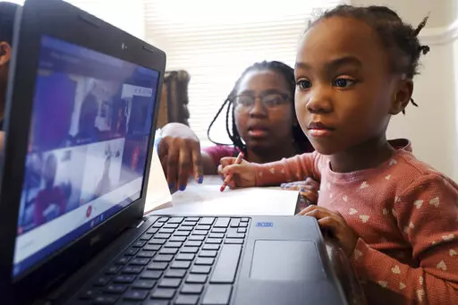 FILE — Lear Preston, 4, who attends Scott Joplin Elementary School, participates in her virtual classes as her mother, Brittany Preston, background, assists at their residence in Chicago's South Side, Feb. 10, 2021. Schools across America are racing to make up for lost classroom time, budgeting billions of dollars for tutoring, summer camps and longer school days. But figuring out which students need help has become its own challenge after the pandemic left holes in some students' learning rec