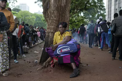 A woman takes a break from the queue outside the passport offices in Harare, Wednesday, Dec. 20, 2023. Atop many Christmas wish lists in economically troubled Zimbabwe is a travel document and people are flooding the passport office this holiday season ahead of a price hike planned in the New Year. The desperation at the office in the capital is palpable as some people fear the hike could push the cost of obtaining a passport out of reach and economic gloom feeds a surge in migration. (AP Photo/