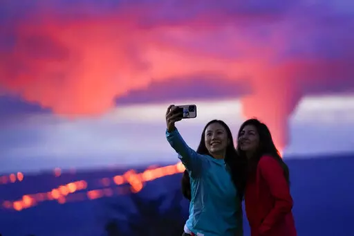 Ingrid Yang, left, and Kelly Bruno, both of San Diego, take a photo in front of lava erupting from Hawaii's Mauna Loa volcano Wednesday, Nov. 30, 2022, near Hilo, Hawaii. (AP Photo/Gregory Bull)
