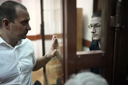 Robert Woodland, right, a Russia-born U.S. citizen, stands in a glass cage as he talks with his lawyer Stanislav Kshevitsky prior to a court hearing, Thursday, July 4, 2024, in Moscow, Russia. Woodland was convicted of drug-related charges and sentenced to 12 and a 1/2 years in prison on Thursday. (AP Photo/Alexander Zemlianichenko)