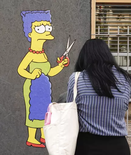 A woman takes pictures of a mural called "The Cut" by street artist aleXsandro Palombo depicting Marge Simpson, a character of the animated television series "The Simpsons" cutting her iconic hair, in front of the Consulate of Iran, in Milan, Italy, Wednesday, Oct. 5, 2022. Thousands of Iranians have taken to the streets over the last two weeks to protest the death of Mahsa Amini, a 22-year-old woman who had been detained by Iran's morality police in the capital of Tehran for allegedly not adher