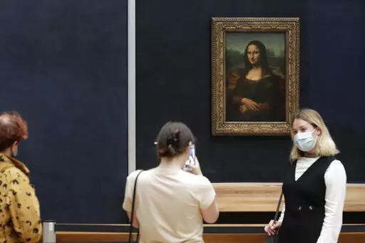 Visitors pose in front of Leonardo da Vinci's Mona Lisa in the Louvre museum, Wednesday, May, 19, 2021 in Paris. A man seemingly disguised as an old woman in a wheelchair threw a piece of cake at the glass protecting the Mona Lisa on Sunday May 29, 2022 at the Louvre Museum and shouted at people to think of planet Earth. (AP Photo/Thibault Camus, File)